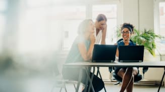 Women smiling at work while looking at computers