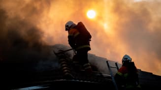 Two firefighters climb ladders onto the roof of a burning building.