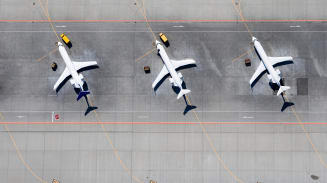 Three planes sit diagonally on a gray airport runway